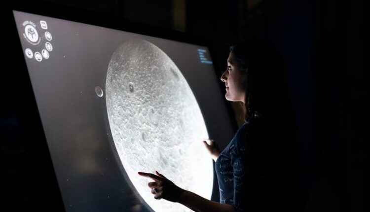 A woman interacts with a touchscreen showing the moon's surface, exploring lunar details.